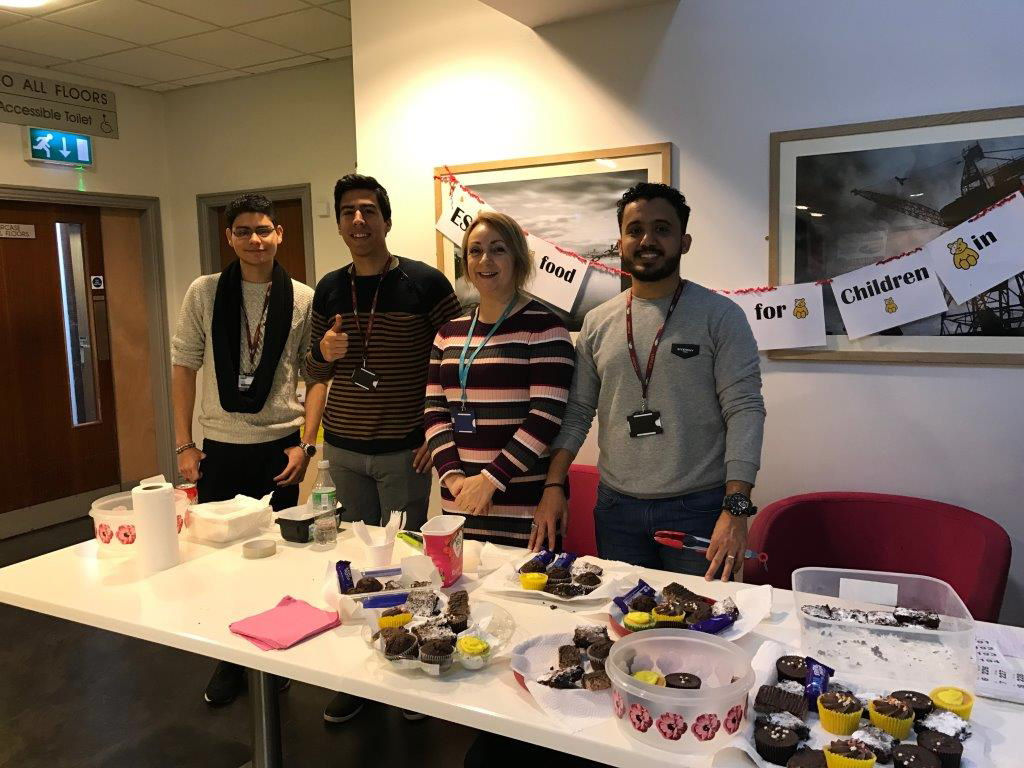 3 Wirral Met Students and 1 Staff Member standing by a table while volunteering for a Children in Need