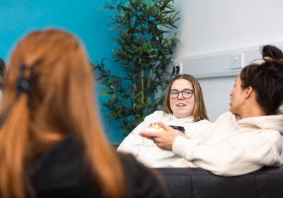 Four Wirral Met Social Studies students sat on a long table working on a blue laptop