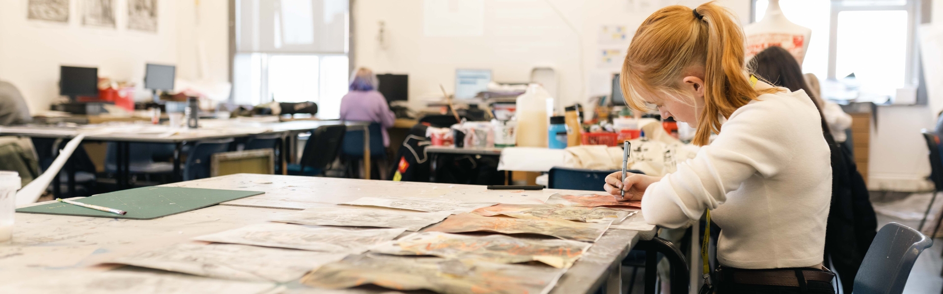 Art & Design student sat at desk drawing inside classroom.