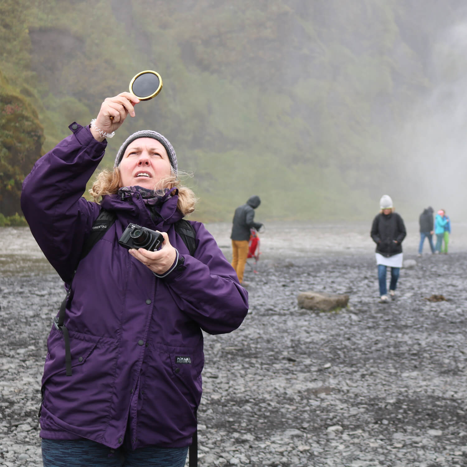 Woman looking through magnifying glass up into the sky with a waterfall and rocks in the background