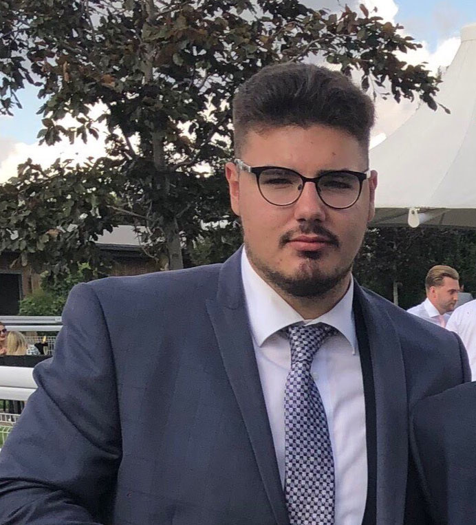 A headshot of new Student Governor Mike Taylor, wearing glasses and a grey suit and tie