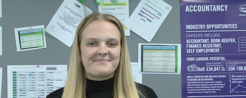 Woman wearing a black jumper standing in front of wall with an accounting poster on it